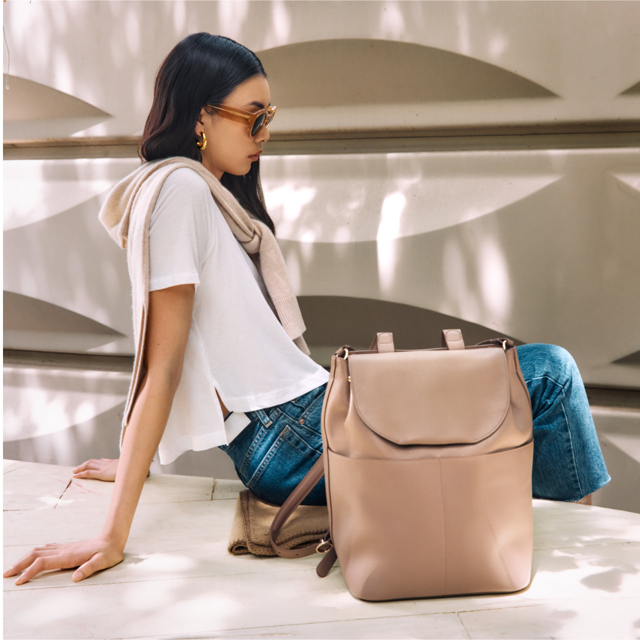 Woman sitting next to a backpack on a sunny day.