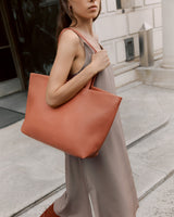 Woman standing outdoors with a large tote bag on her shoulder.