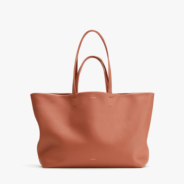 Large leather tote bag with two handles standing upright.