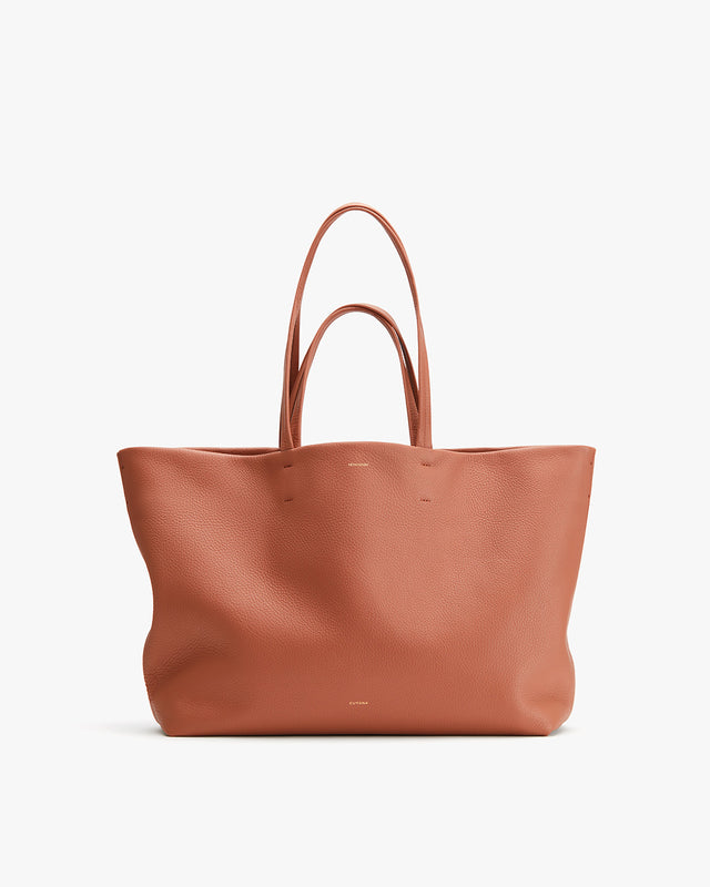 Large leather tote bag with two handles standing upright.