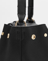 Close-up of a handbag with metallic details and a handle attached by rings.