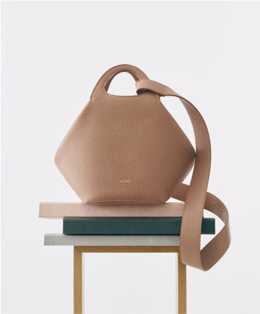 Handbag with a wide strap on a stack of books on a wooden table.