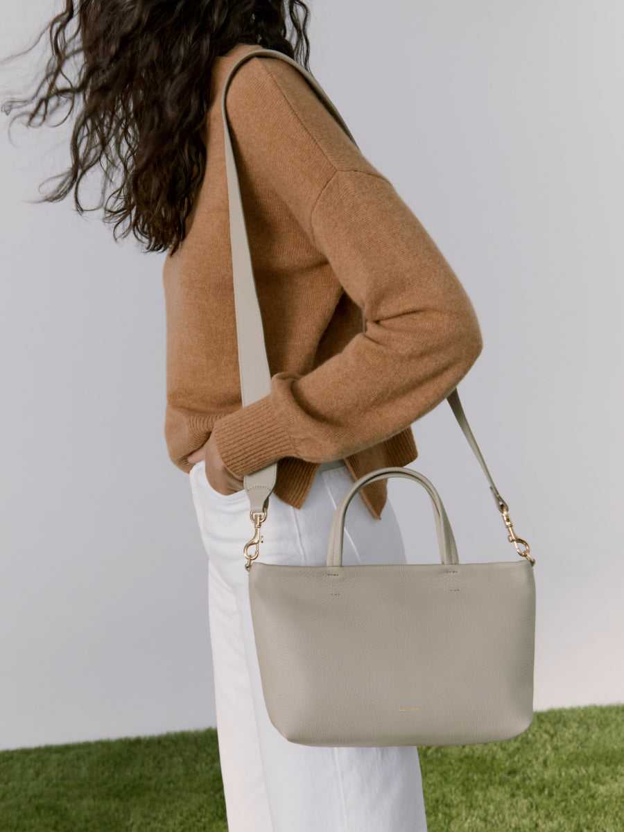 Woman with curly hair holding a handbag, viewed from behind.