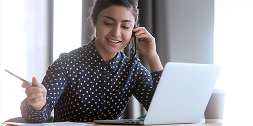 An employee works on her laptop while talking on the phone.