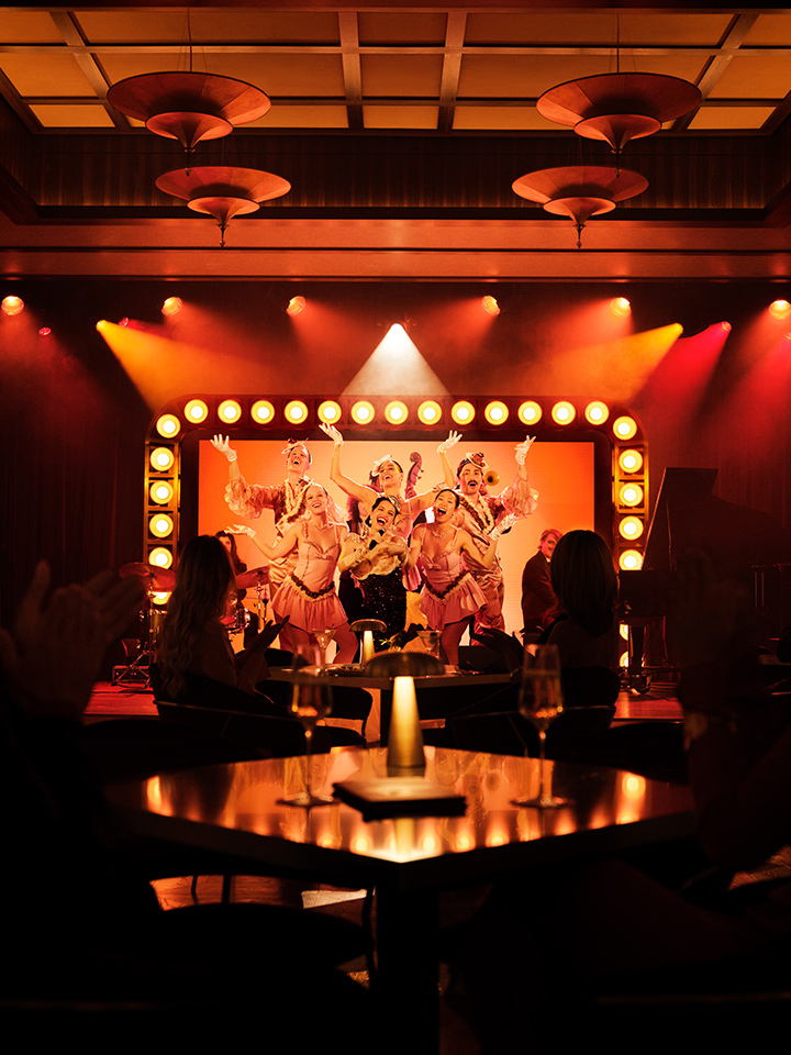 Nightcap interior shot, red lights in a dark room. The angle is sitting at a table facing the stage