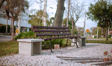 Praça com banco e árvores ao fundo.