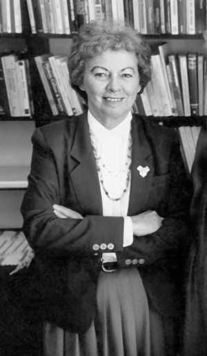 Nel Noddings standing with crossed arms in front of shelves of books