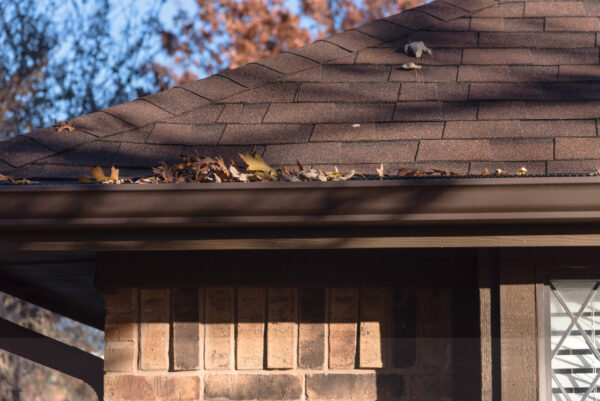 Close up rain gutter on residential home clogged with dried fall leaves.