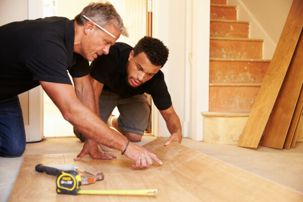 Two men laying wood panel flooring in a house