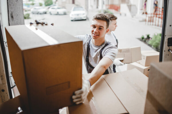 young smiling mover unpacking boxes from van