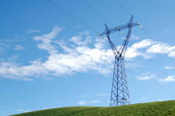 Electric Transmission lines on a green hill with a blue sky background