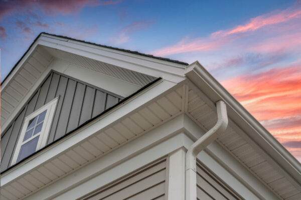 White frame gutter guard system, with gray horizontal and vertical vinyl siding fascia, drip edge, soffit, on a pitched roof attic at a luxury American single family home