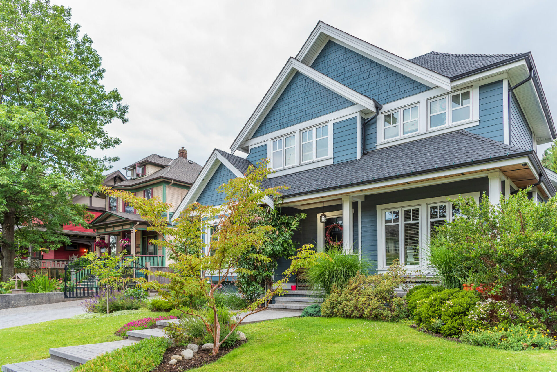 Blue house with front porch, large green lawn, and green shrubs.