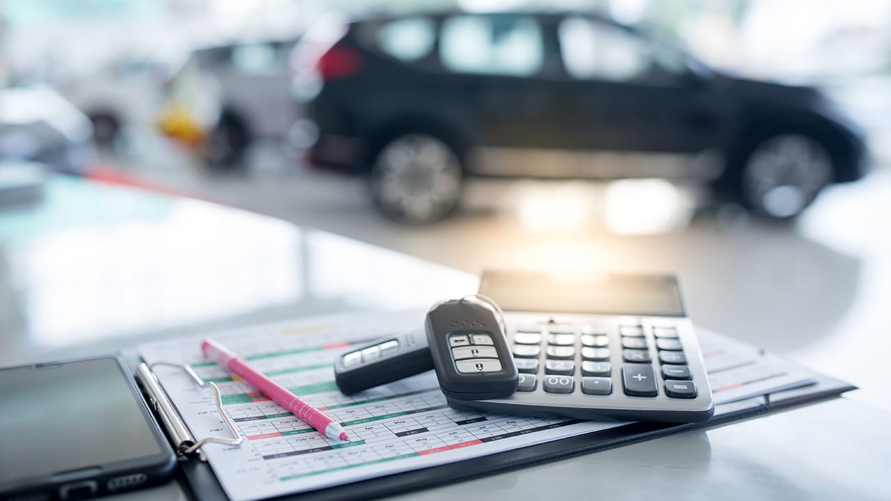 New key - images of car showrooms with calculators and two new remote keys placed on the work table in the new car showroom. The background is a car showroom.