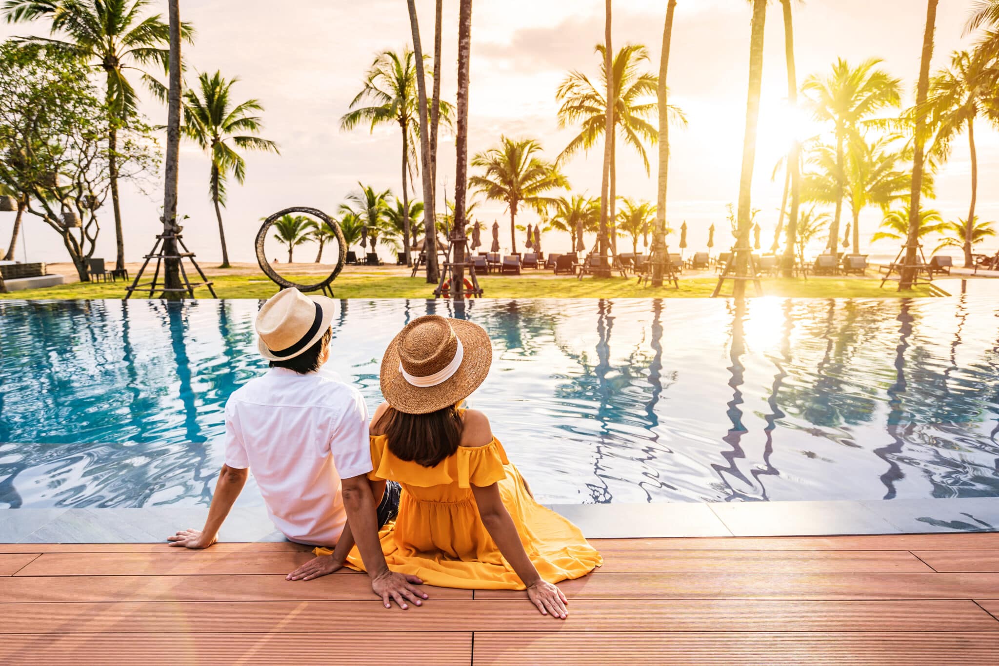 Young couple traveler relaxing and enjoying the sunset by a tropical resort pool while traveling for summer vacation