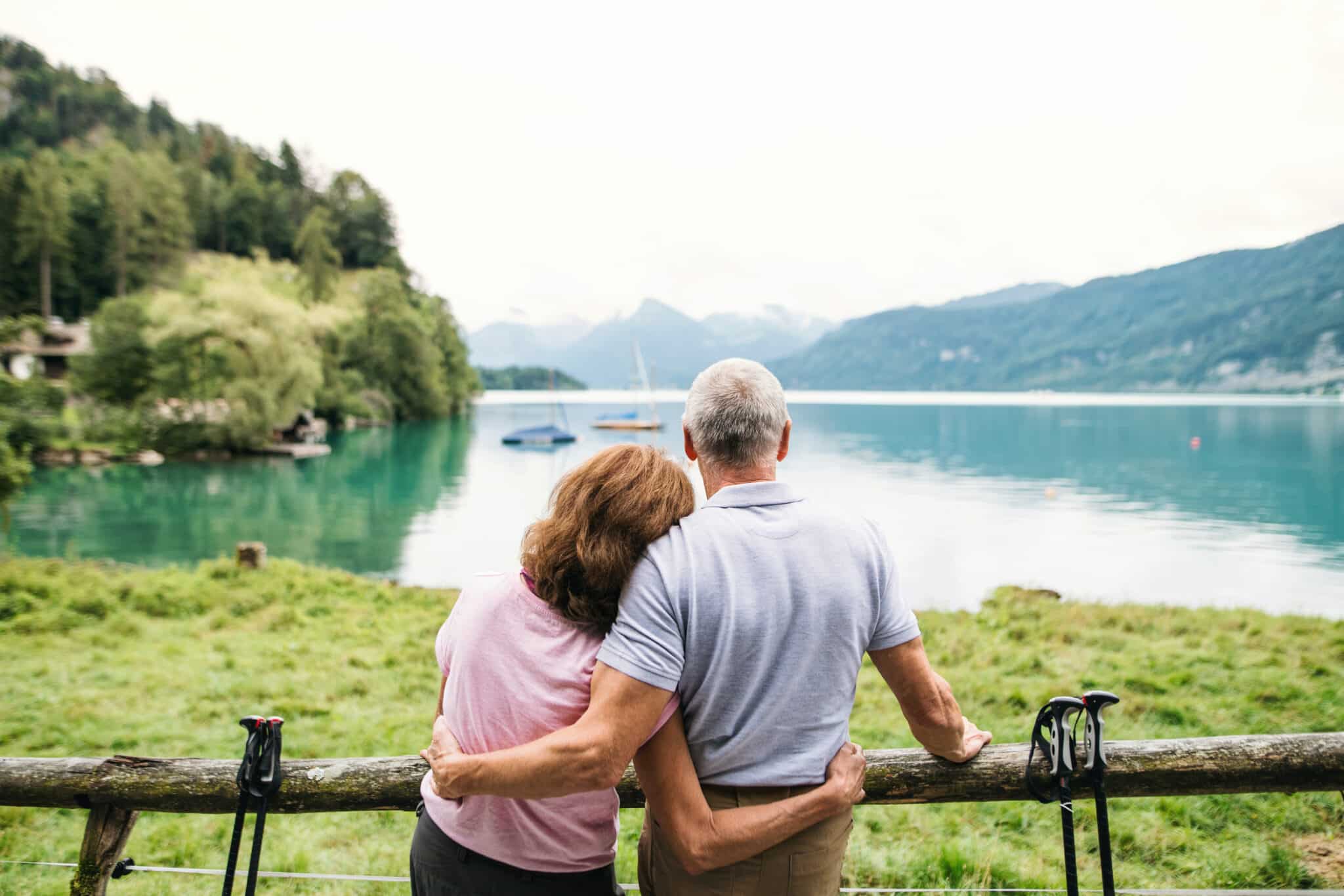 A rear view of senior pensioner couple standing by lake in nature.