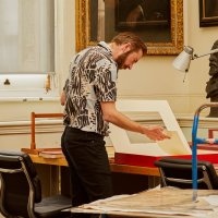 Zorian Clayton inspects a print in a room surrounded by various different artworks