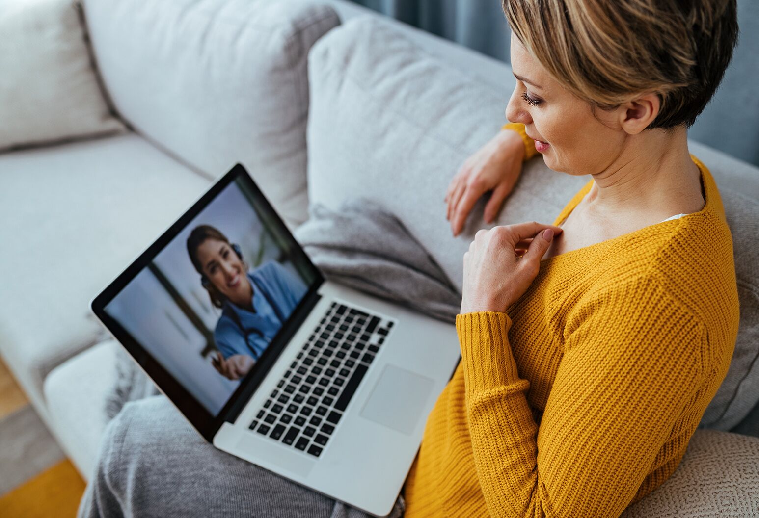 Young woman sitting on the sofa while talking with her doctor over a laptop.