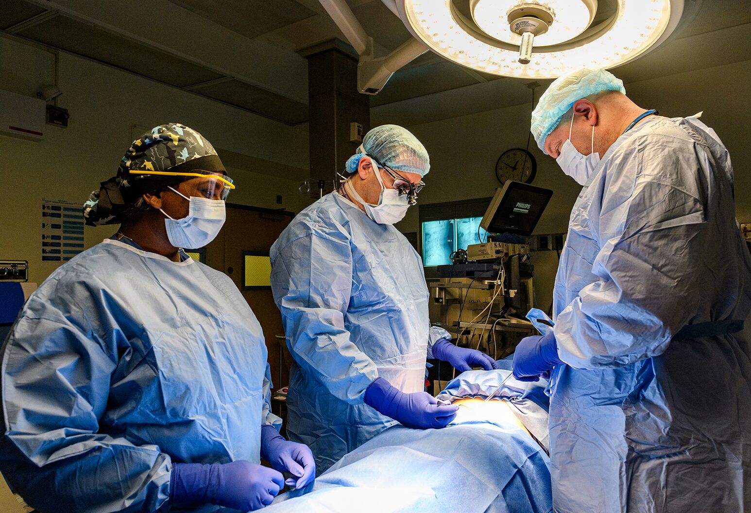 Several surgeons examine the body of a patient on a surgical table in an operating room.