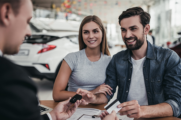 couple getting car key from car dealer in showroom and signing contract