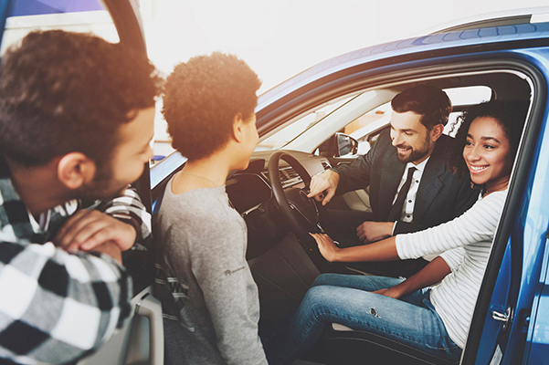 Family at car dealership. Salesman is showing new car.