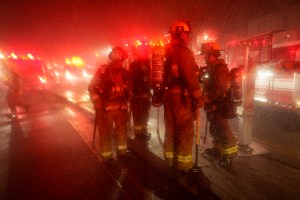 Firefighters stand in the middle of several fire trucks.