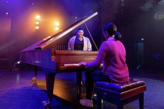 First Nations student singing on stage accompanied by another student playing piano