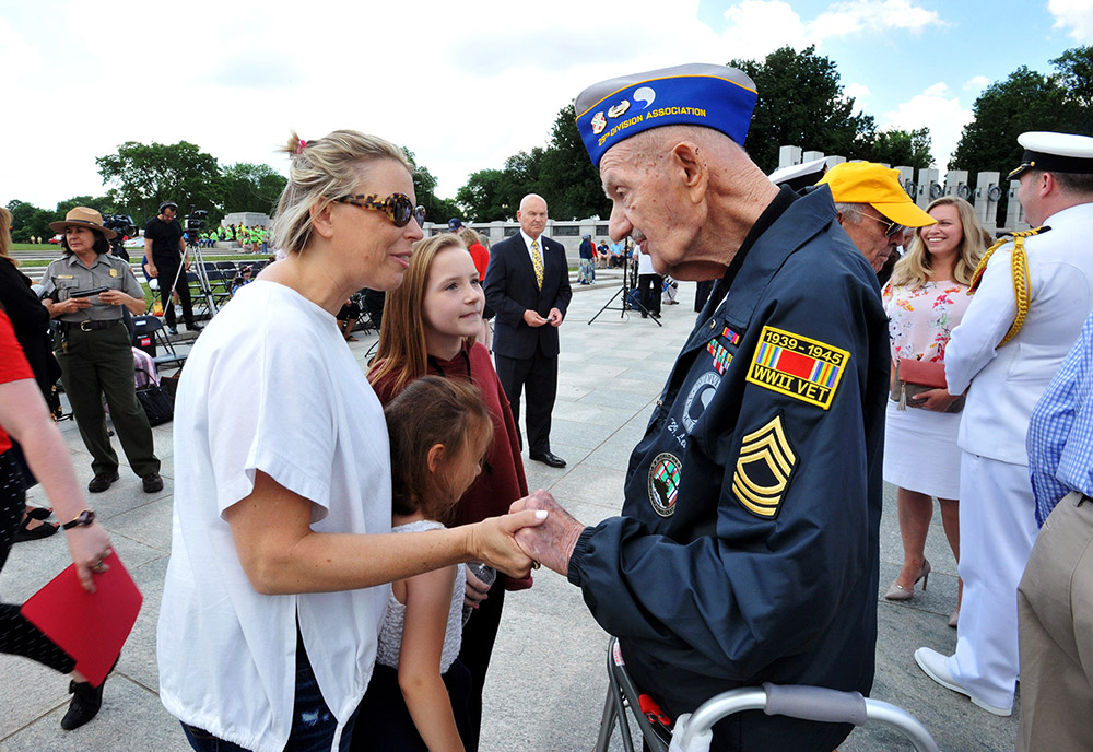 World War II Veteran speaking with a mother and two daughters at the World War II monument in Washington, DC.