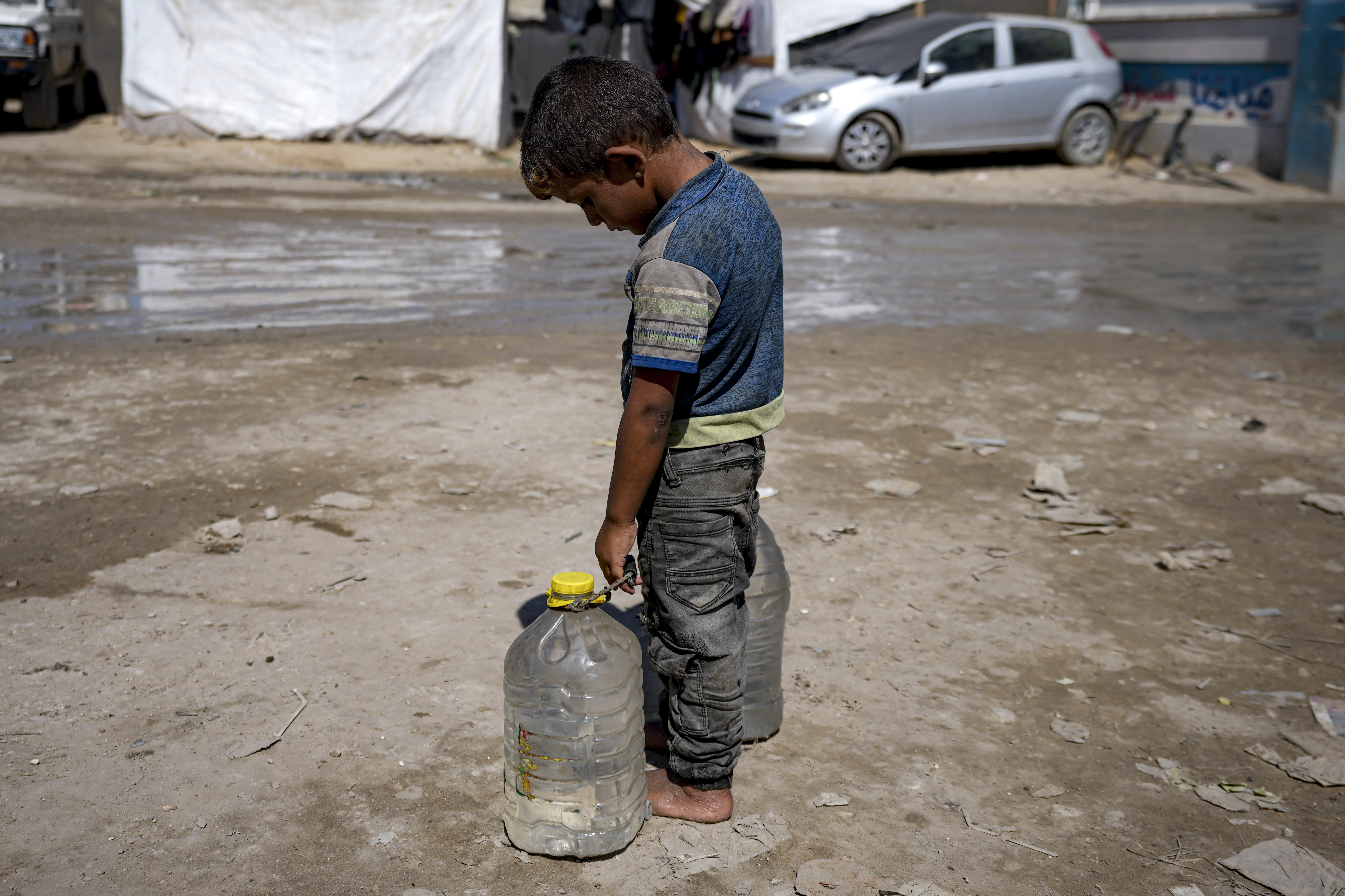 A displaced child carries filled water bottles at a makeshift tent camp in Deir al-Balah, central Gaza Strip, Thursday, Aug. 29, 2024. (AP Photo/Abdel Kareem Hana)