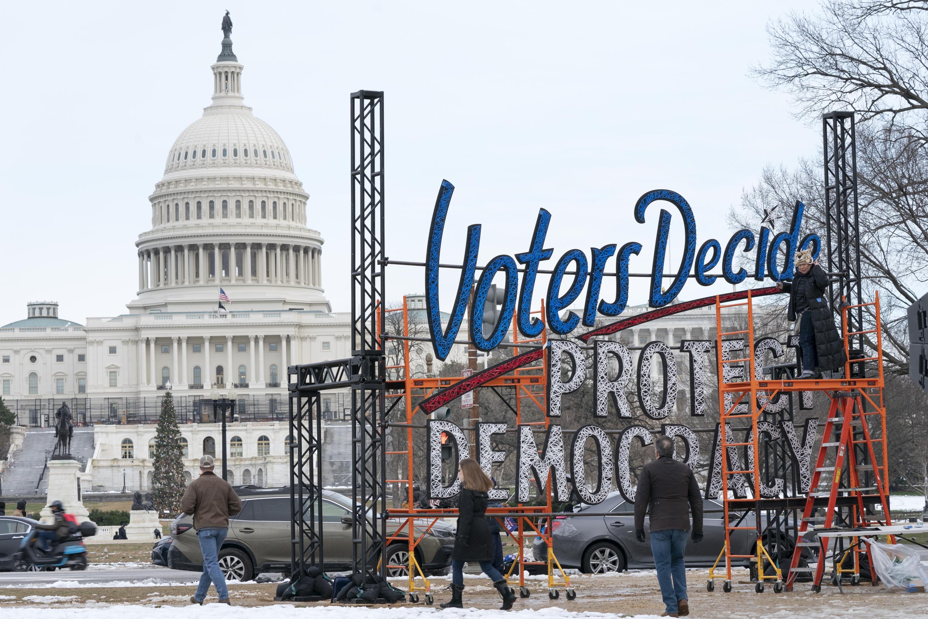 FILE - With the U.S. Capitol in the background, people walk past a sign that says say, "Voters Decide Protect Democracy," Jan. 6, 2022, in Washington. This week’s ballot had an unspoken candidate, American democracy. Two years of relentless attacks on democratic traditions by former President Donald Trump and his allies left the country's future in doubt, and voters responded. Many of the candidates who supported the lie that Trump won the 2020 election lost races that could have put them in a position to influence future elections. But the conditions that threatened democracy's demise remain, and Americans view them from very different perspectives. (AP Photo/Jacquelyn Martin, File)