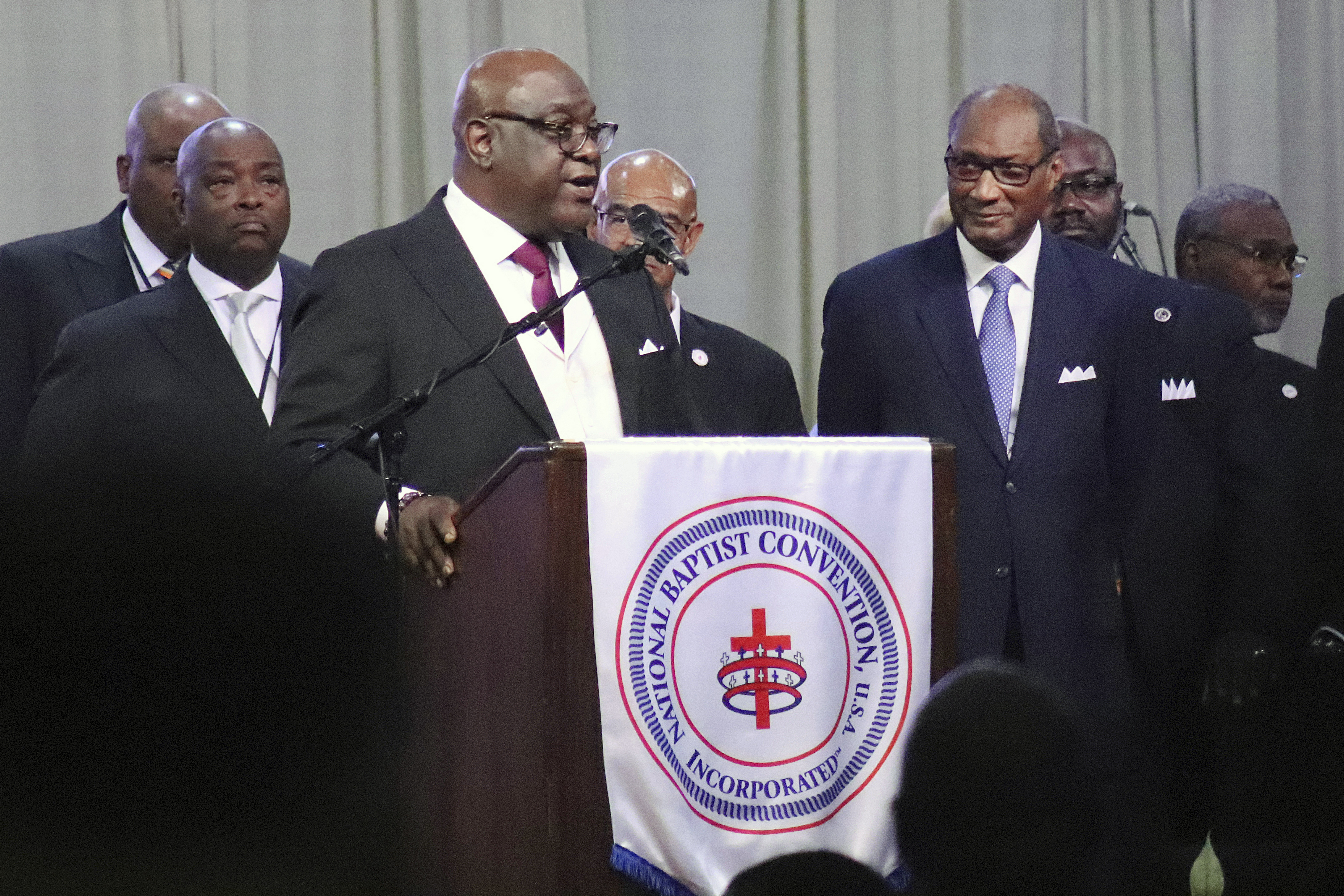 The Rev. Boise Kimber, at podium, president-elect of the National Baptist Convention, USA, addresses the group's annual meeting at the Baltimore Convention Center in Baltimore, Md., on Thursday, Sept. 5, 2024. The Rev. Jerry Young, outgoing NBCUSA president, stands at foreground right. (Adelle M. Banks/RNS via AP)