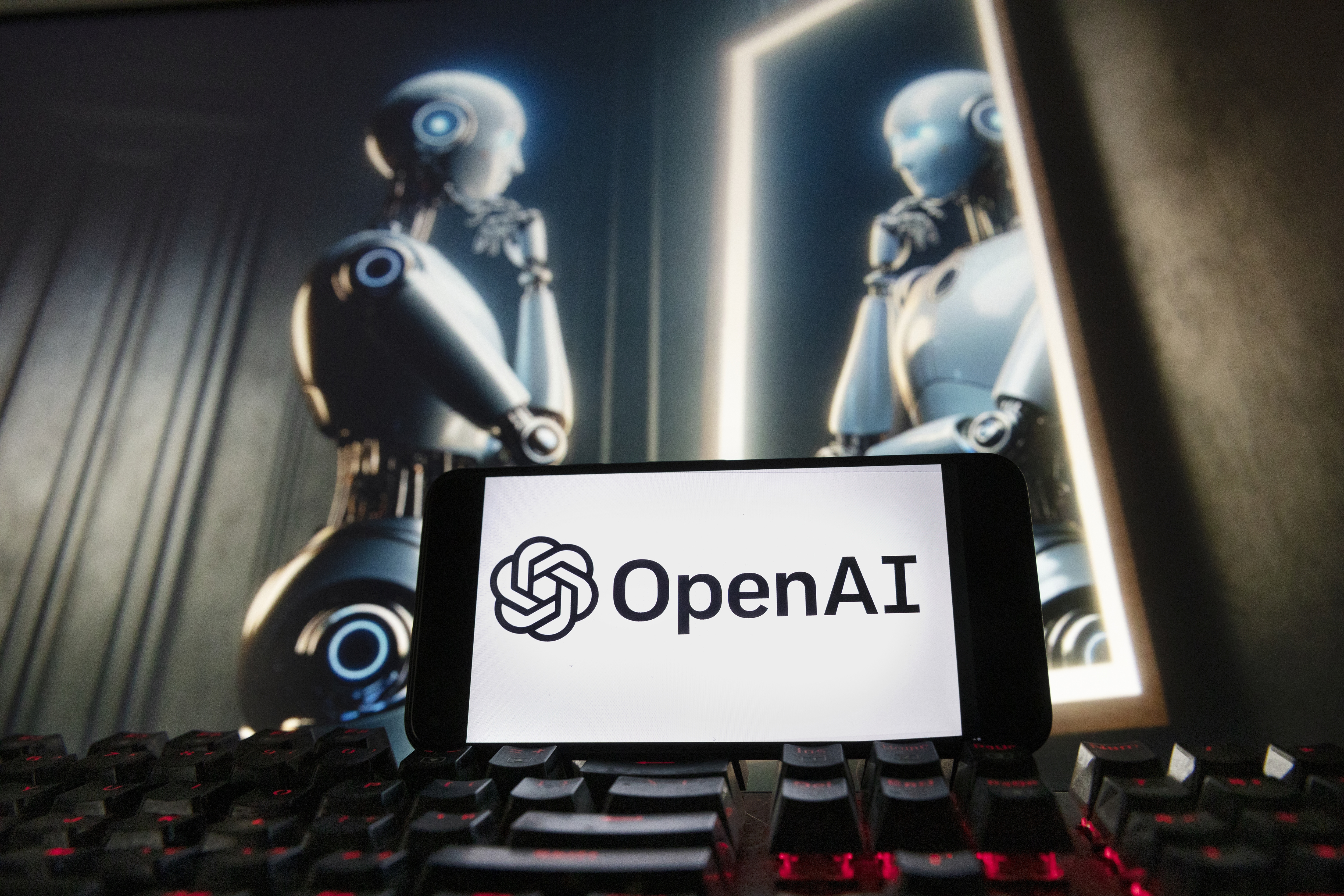 FILE- The OpenAI logo is displayed on a cell phone with an image on a computer monitor generated by ChatGPT's Dall-E text-to-image model, Dec. 8, 2023, in Boston. lya Sutskever, one of the founders of OpenAI who was involved in a failed effort to push out CEO Sam Altman, said he's starting a safety-focused artificial intelligence company. Sutskever, a respected AI researcher who left the ChatGPT maker last month, said in a social media post on Wednesday, June 19, 2024 that he's setting up Safe Superintelligence Inc. with two co-founders. (AP Photo/Michael Dwyer, File)