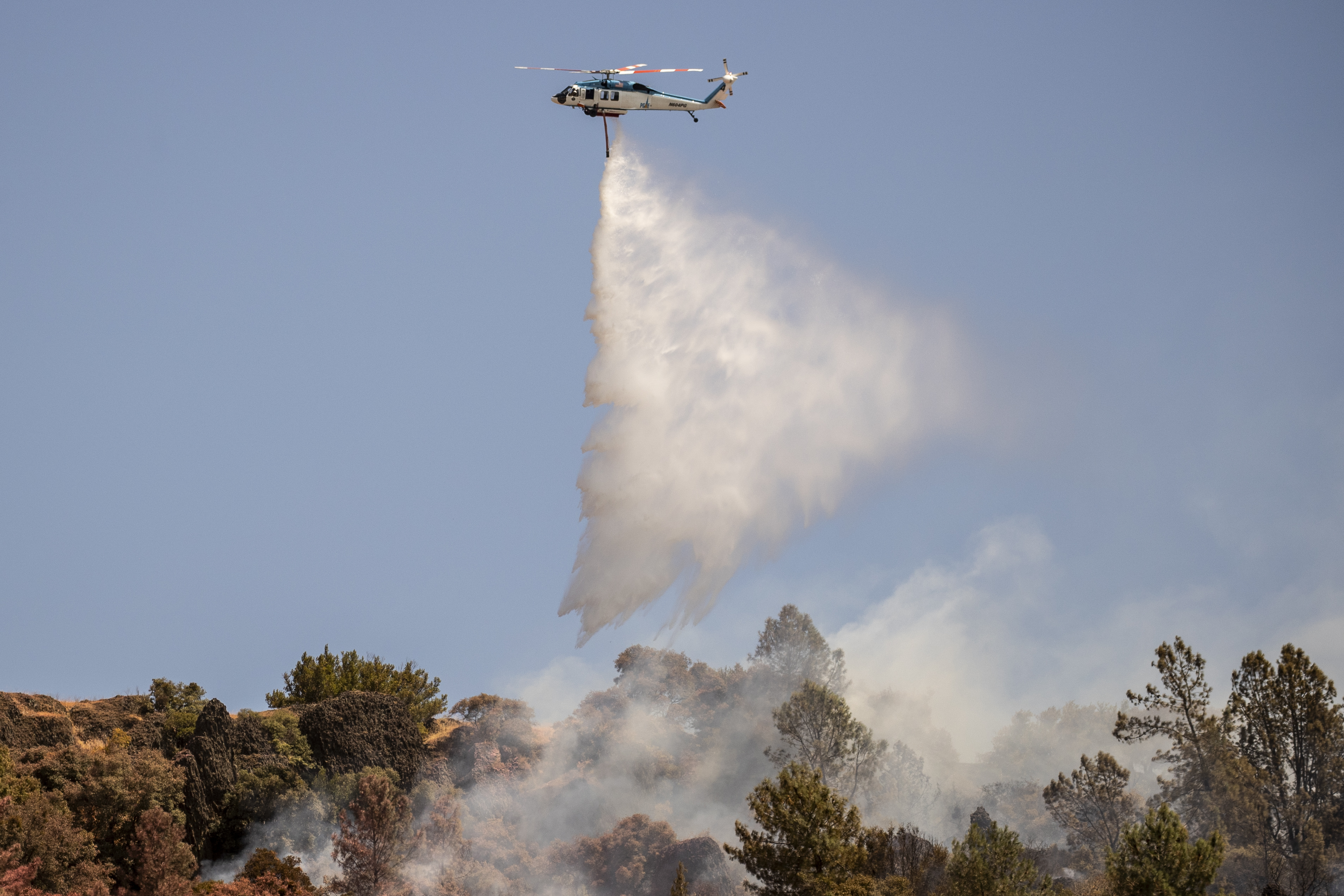 A Pacific Gas and Electric Company (PG&E) firefighting helicopter releases water over a hot spot while battling the Thompson Fire, in Oroville, Calif., Wednesday, July 3, 2024. (Stephen Lam/San Francisco Chronicle via AP)