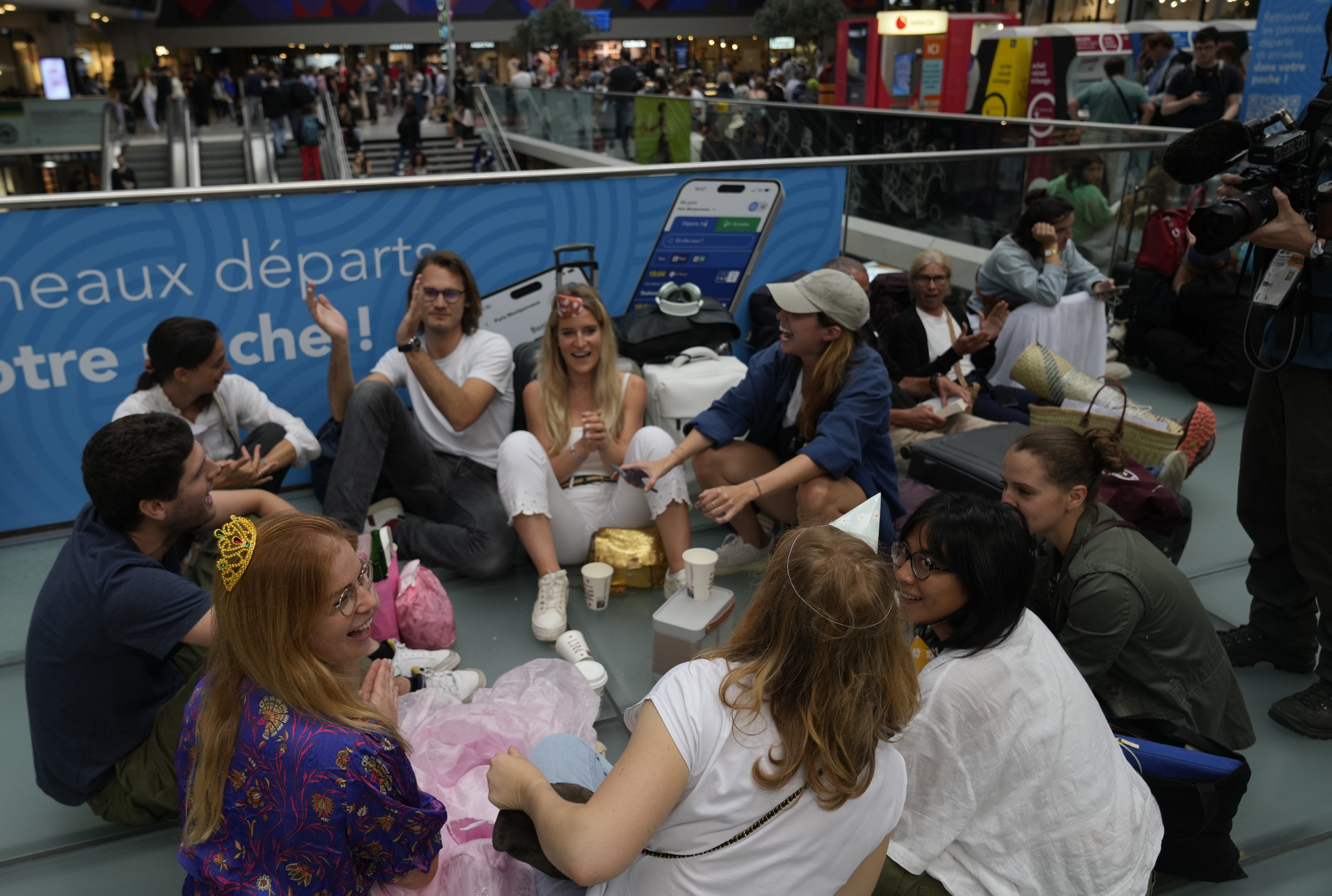 Travelers sit at the Gare de Montparnasse, at the 2024 Summer Olympics, Friday, July 26, 2024, in Paris, France. Hours away from the grand opening ceremony of the Olympics, high-speed rail traffic to the French capital was severely disrupted on Friday following what officials described as "criminal actions" and sabotage AP Photo/Yasin Dar)