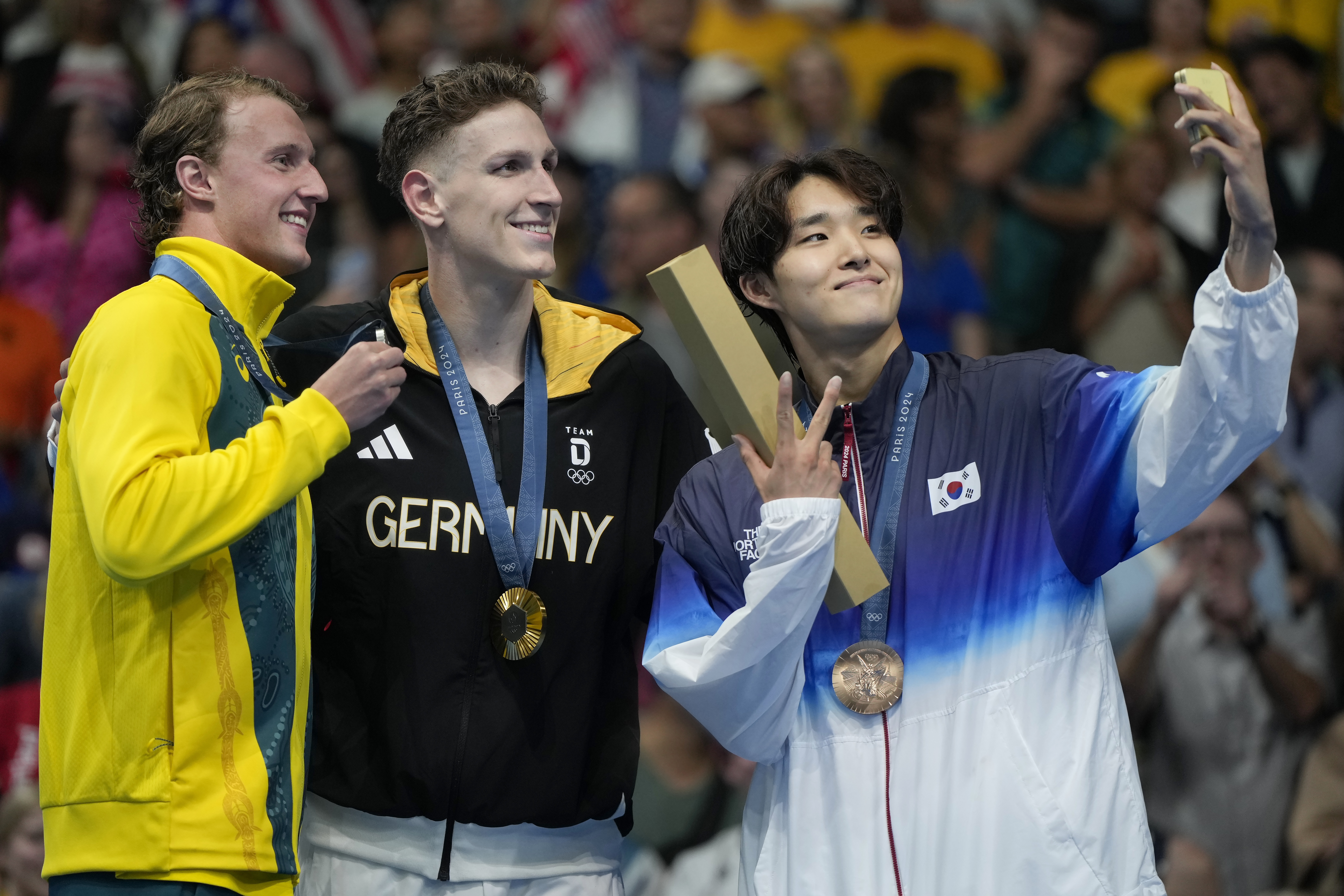 FILE - Gold medalist Lukas Maertens, of Germany, middle, poses with silver medalist Elijah Winnington, of Australia, left, and bronze medalist Kim Woo-min of South Korea, on the podium after the men's 400-meter freestyle final at the 2024 Summer Olympics, July 27, 2024, in Nanterre, France. Swimming Australia has fired coach Michael Palfrey over comments made at the Paris Olympics where he said he hoped a South Korean athlete would beat Australian swimmers. (AP Photo/Matthias Schrader, File)