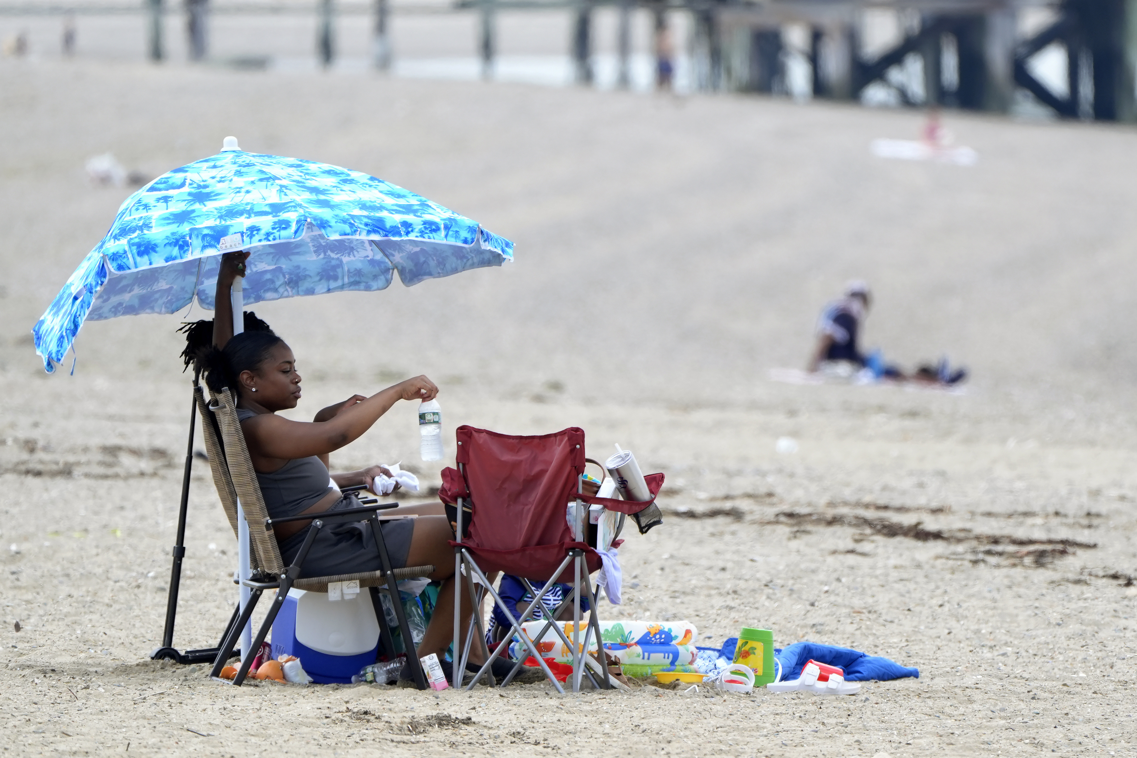 Sierra Payne, of Boston, reaches for a bottle of water while trying to stay cool under an umbrella as she visits Wollaston Beach, Monday, July 15, 2024, in Quincy, Mass. Temperatures reached 90 degrees in many areas in the state Monday. (AP Photo/Steven Senne)