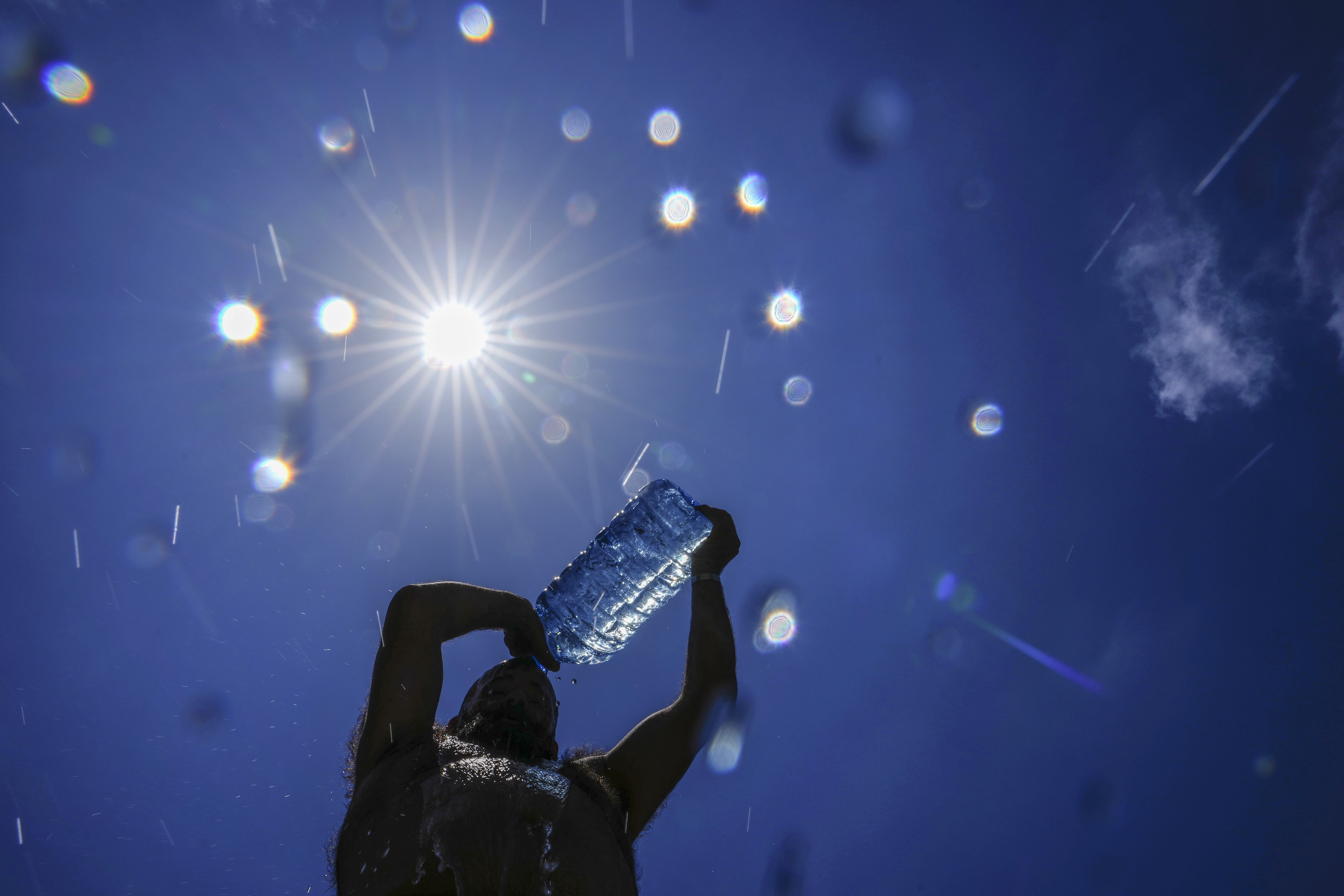 FILE - A man pours cold water onto his head to cool off on a sweltering hot day in the Mediterranean Sea in Beirut, Lebanon, July 16, 2023. As temperatures and humidity soar outside, what's happening inside the human body can become a life-or-death battle decided by just a few degrees. (AP Photo/Hassan Ammar, File)