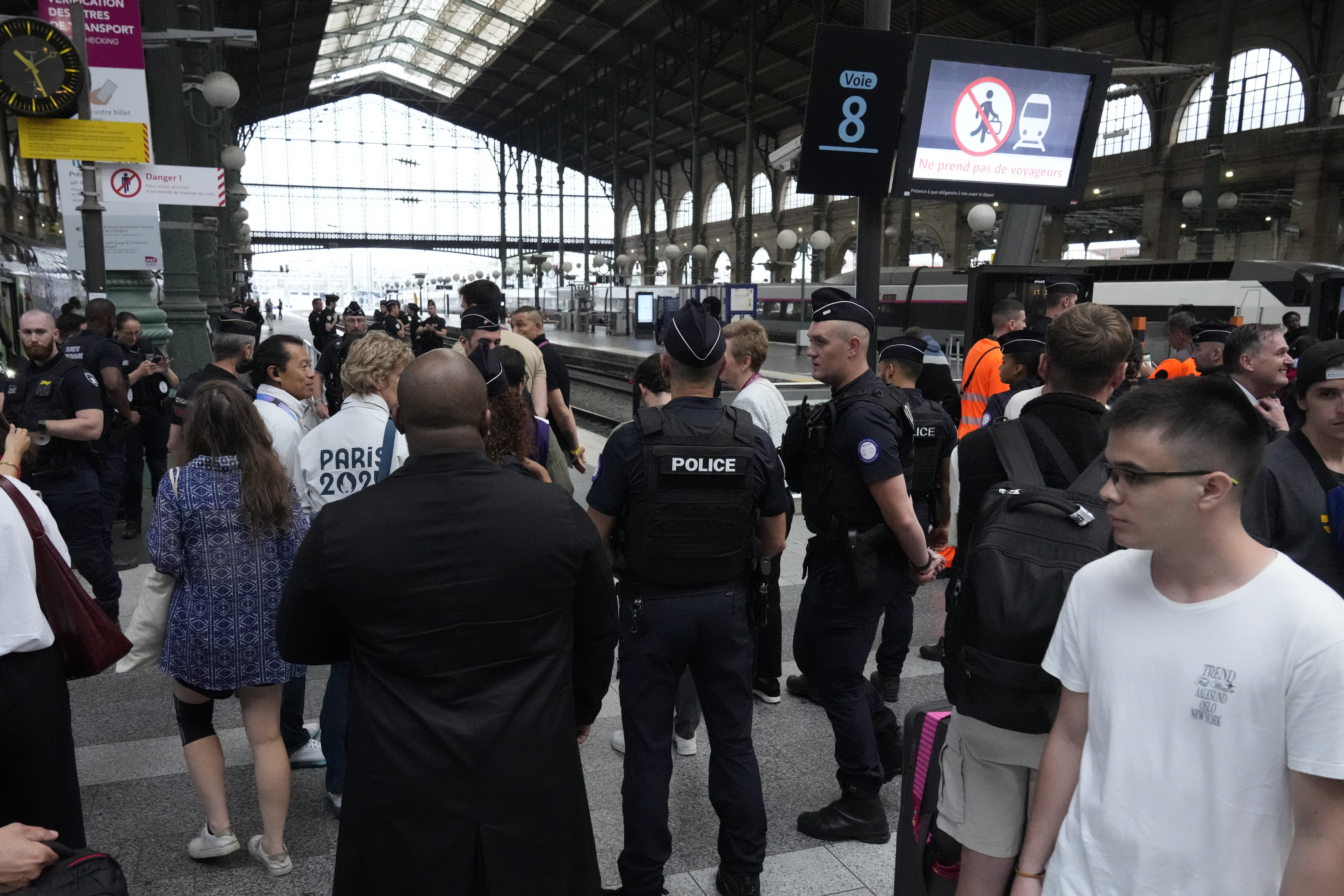 Travelers wait as police officers patrol inside the Gare du Nord train station at the 2024 Summer Olympics, Friday, July 26, 2024, in Paris, France. Hours away from the grand opening ceremony of the Olympics, high-speed rail traffic to the French capital was severely disrupted on Friday by what officials described as "criminal actions" and sabotage. (AP Photo/Mark Baker)