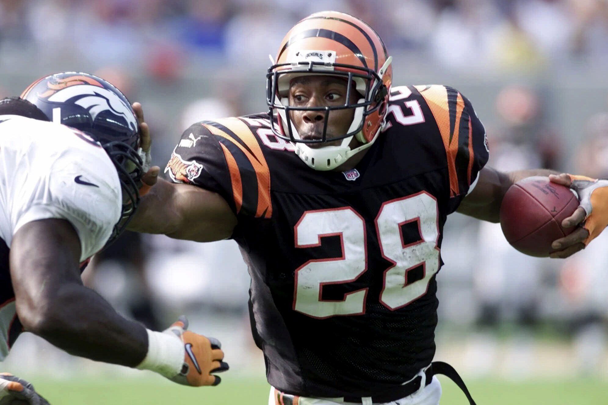 FILE - Cincinnati Bengals running back Corey Dillon (28) pushes away Denver Broncos defender Al Wilson, left, in the first half Sunday, Oct. 22, 2000, in Cincinnati. The Cincinnati Bengals are adding running back Corey Dillon and nose tackle Tim Krumrie to the team's Ring of Honor this fall. (AP Photo/Al Behrman, File)