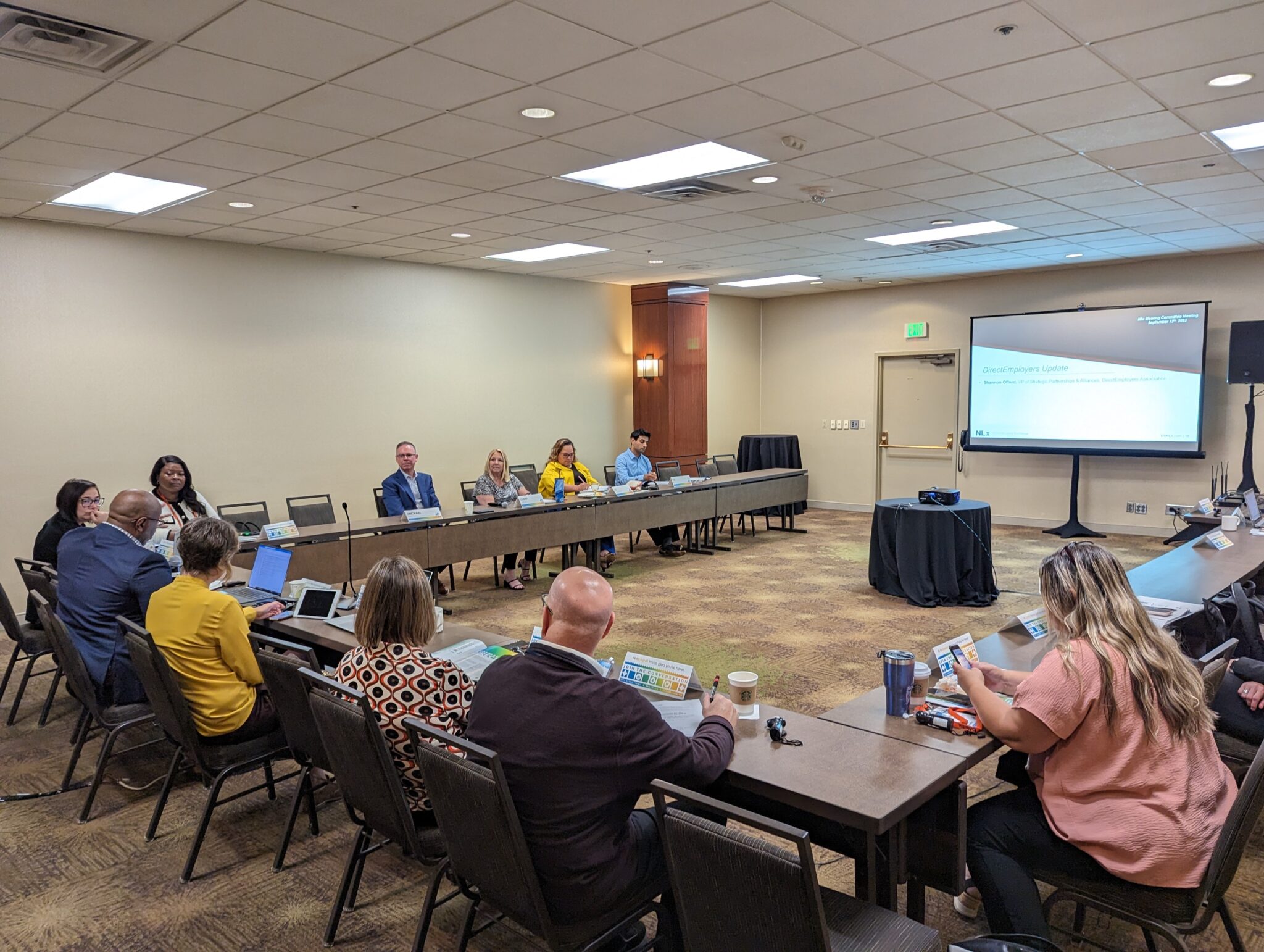 Group of people sitting at a U shaped table discussing a slide that is being shown