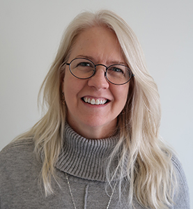 Teri Sparks is a White woman with long white hair. She smiles brightly with black thin rimmed glasses. She is wearing a light grey sweater.