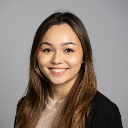 Julia Nguyen is a young Asian woman with long brown hair. She smiles brightly and wears a light tan blouse under a black blazer.