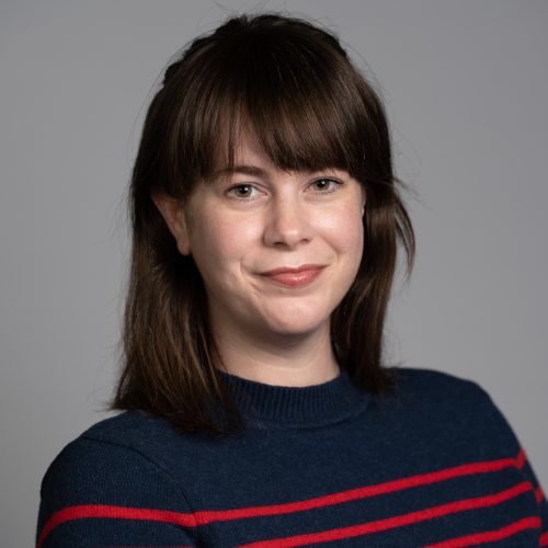 Lucy Caltagirone is a young White woman with shoulder length dark brown hair with bangs. She smiles and wears a navy top with thin red stripes.