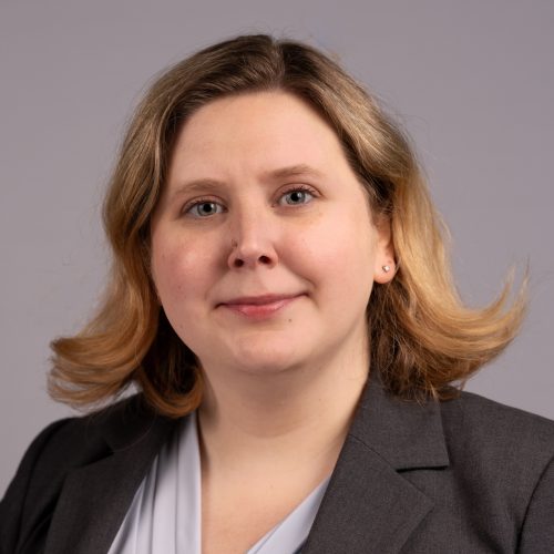 Portrait of Randi Ames, a white woman with blonde hair, wearing a dark grey blazer and light grey blouse.