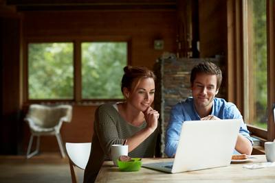 Smiling young couple using laptop while having coffee at table in cottage