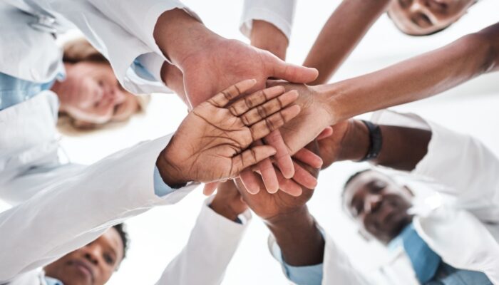 group of doctors in a circle with their hands meeting in the middle to symbolize teamwork, focus is on the underside of the group and hands