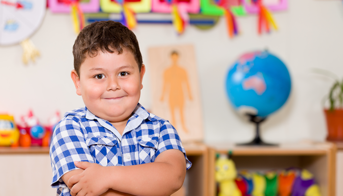 Young boy in school classroom smiling with his mouth closed and crossing his arms across his chest