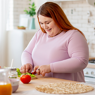 Woman standing at kitchen counter smiling and cutting lettuce and tomatoes