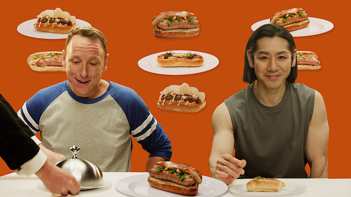 Joey Chestnut and Takeru Kobayashi sitting next to each other in front of a hot dog on a serving platter. 