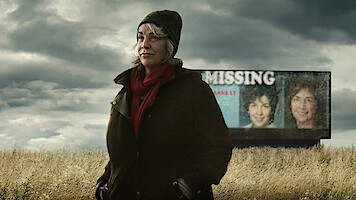 Cathy Terkanian standing in a field with a missing persons billboard in the background.